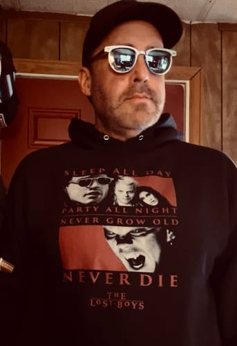 A customer poses in the black Never Die Lost Boys Hoodie, showing the film-themed graphic on the front.