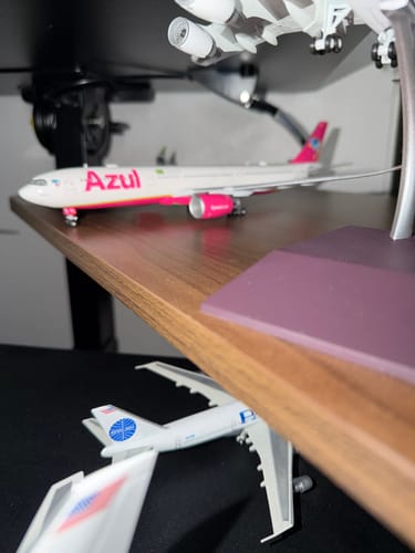 Reviewer's pink and white Azul A330-900neo model airplane displayed on a wooden shelf with other models.
