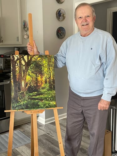 Reviewer stands beside an easel displaying their finished, vibrant Forest Scene painting.