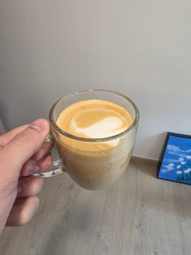 Reviewer holds a clear glass mug with a creamy latte made from Kiwi Candy coffee.