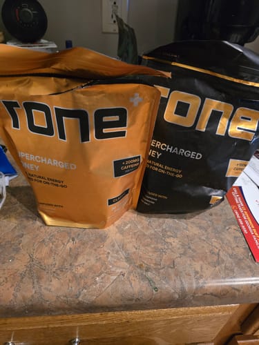 Customer's orange bag of SuperCharged Honey next to another black bag on a countertop.