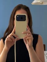 Cliente tirando uma foto no espelho com seu celular, mostrando a case Odara na cor creme e sua alça.