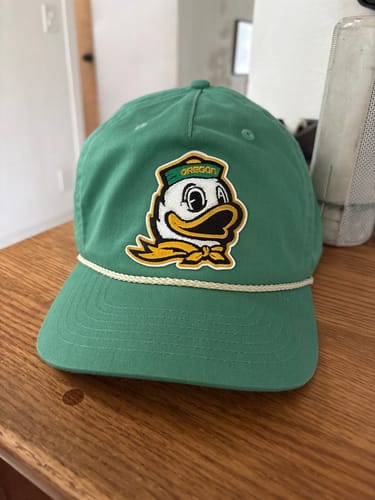 Customer's green unstructured rope hat with a custom Oregon duck patch on the front, sitting on a wooden table.