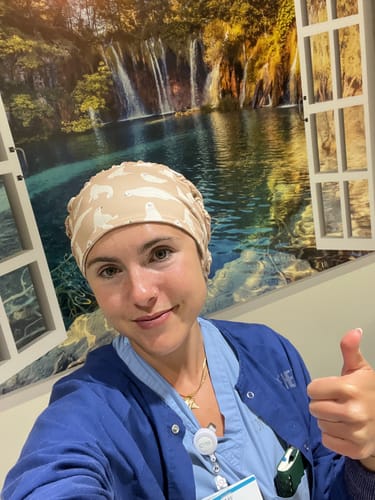 Reviewer in blue scrubs gives a thumbs-up while wearing the DuoStyle Scrub Hat with a seals pattern.