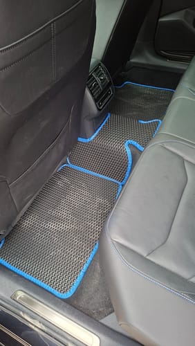 Klienta czarne dywaniki samochodowe z niebieskim obszyciem, zamontowane na tylnej podłodze samochodu.