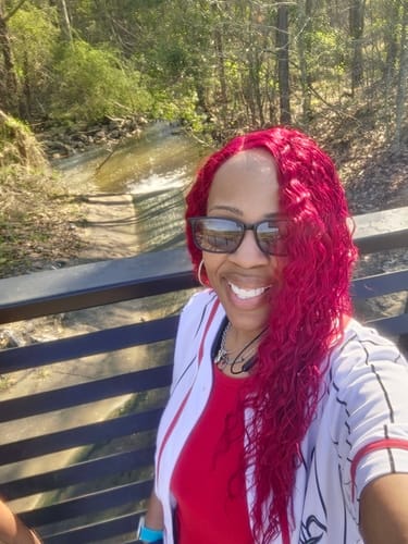 Reviewer smiling outdoors, wearing the long, bright red SWISS LACE QUINNIE wig.