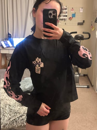 Customer takes a mirror selfie wearing the black Flaming Disaster Long Sleeve, showing the pink flame graphics on the sleeves.