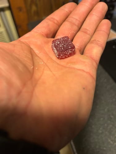 Reviewer holding a single, sugared Blackberry Yuzu Live Resin Gummy in their palm.