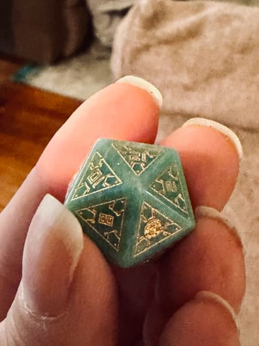 Close-up: Reviewer holding a green Peruvian Amazonite d20 die with gold details.