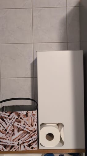 Anmelders hvite toalettpapirstativ på en hylle på badet, med én dorull synlig.