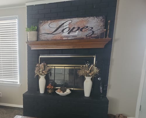 Customer's rustic 'Lopez' family name sign canvas displayed on a wooden mantel above a black brick fireplace.