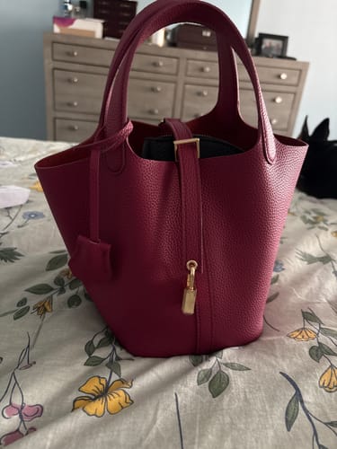 Customer's magenta Picolle Leather Bag with gold hardware shown resting on a floral patterned surface.