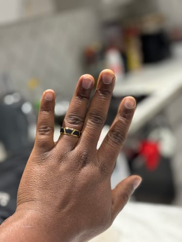 Customer's hand wearing the black and gold Magnar ring on their finger against a blurred indoor background.