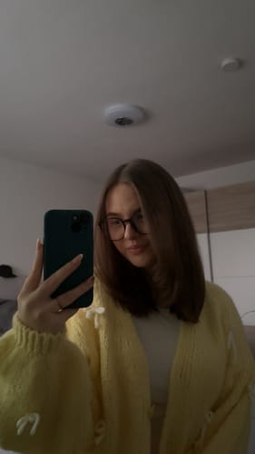 Kundin in einer Nahaufnahme, die den gelben Oversize Mini Schleifen Cardigan mit kleinen Schleifen trägt.