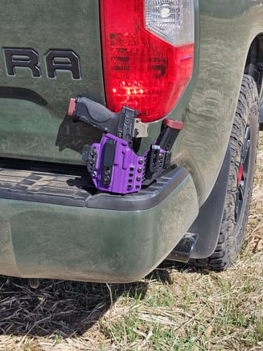 Customer's purple APX holster with a handgun and magazine carrier, displayed on the back of a green truck.