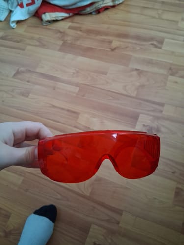 Customer holding their pair of red VisionX glasses over a wood floor.
