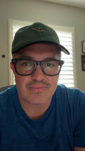 Reviewer wearing the green The Land Before Time 'Me Can Fly!' dad hat indoors.