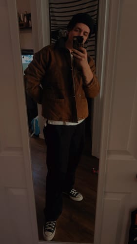 Customer takes a mirror selfie showing the relaxed fit of the brown Fireman Clasp Jacket indoors.