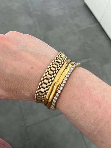 Customer shows their Luxe Tennis Bracelet with sparkling stones, worn in a gold bracelet stack.