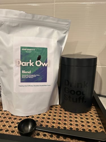 Reviewer's bag of 'Dark Owl Blend' coffee from their subscription, placed with a black canister and scoop.