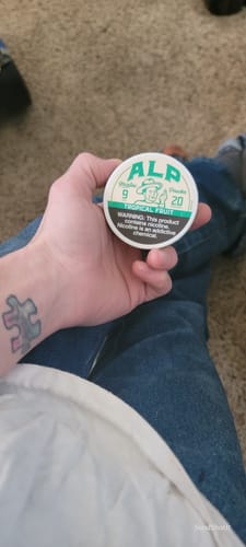 Reviewer holding a round can of ALP Tropical Fruit 9mg Nicotine Pouches in their hand.