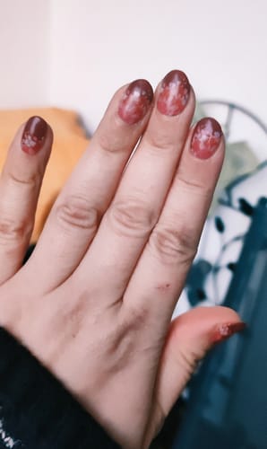 Kundin zeigt ihre Nägel mit den scharlachroten 'Dipped In Blooms' UV-Gel-Nagelfolien mit Blumenmuster.