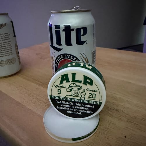 A customer's can of ALP Mountain Wintergreen Nicotine Pouches, showing the 9mg label, on a wooden table.