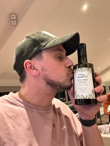 Recensent kysser en flaska Extra Virgin Olivolja från ArcticMed inomhus.