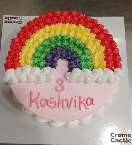 Customer's personalized Rainbow Cream Cake with colorful piped frosting forming a rainbow over a light pink base.