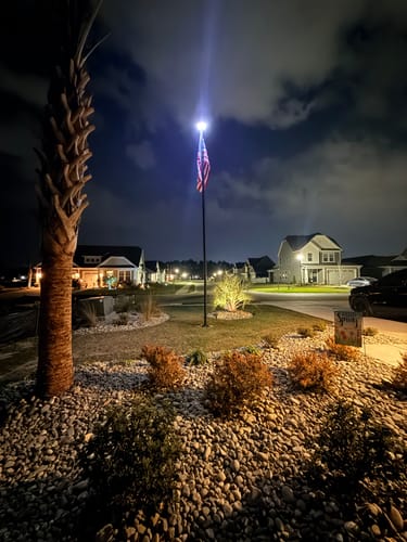 Customer's illuminated Ultra Heavy-Duty Home Flagpole shown at night in their landscaped yard.