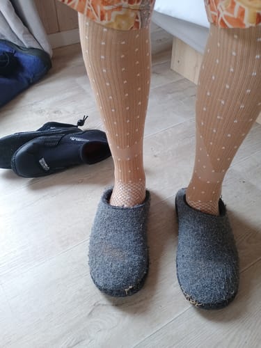 Anmelder har de lysebrune, prikkede støttestrømper på med et par hjemmesko.