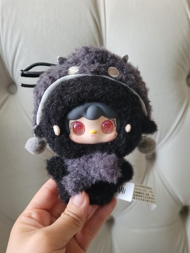 Customer holding a dark, fuzzy Yooki Starlit Traces Series Plush against a light grey tufted background.