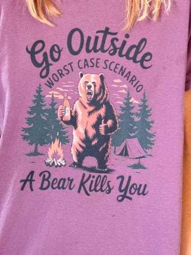 Close-up of a customer wearing the purple 'Go Outside' t-shirt with its funny graphic of a bear at a campsite.
