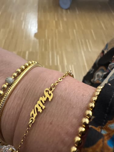 Kundin trägt ihr goldenes personalisierbares Armband am Handgelenk, kombiniert mit anderem Schmuck.