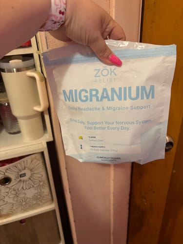 Reviewer's hand holding the white and blue pouch of Migranium Daily.