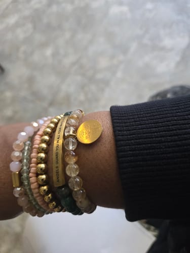 Reviewer's wrist with a stack of beaded bracelets, including the gold 'Angels Guard You' bar bracelet.