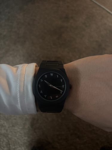 Reviewer wearing the black Lucky Fours® Aura watch on their wrist, showing the face with Arabic numerals.