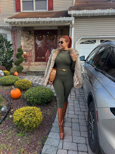 Reviewer walking outside in a form-fitting olive Naked Closed Toe Jumpsuit, styled with a coat and boots.