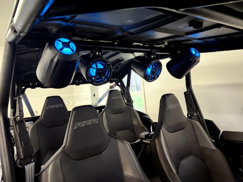 Customer's four black NUTV5 QUAD PRO speakers installed on a UTV roof, with bright blue LEDs illuminating the cabin.