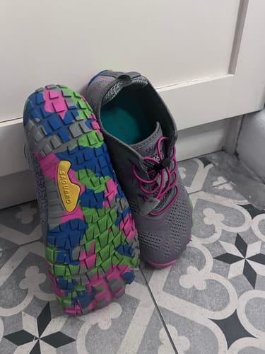Kunde zeigt die grauen Smart II Barfußschuhe, wobei die bunte, gemusterte Sohle eines Schuhs zu sehen ist.