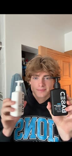 Reviewer holding the white and black pump bottles of the Daily Skincare Duo in a bathroom.