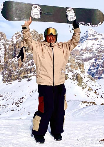 Customer wearing the baggy multi-pocket corduroy snow pants on a snowy mountain, holding up a snowboard.