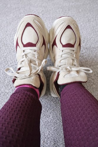 Ein Kunde zeigt die Essential Chunky Sneaker aus der Vogelperspektive an den Füßen, passend zu einer weinroten Leggings.