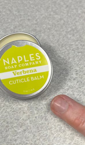 Reviewer showing Verbena Cuticle Balm applied to their finger next to the open tin.