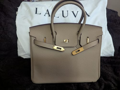 Customer's taupe LALUVA Warkin Bag with gold hardware, shown in front of its branded dust bag.