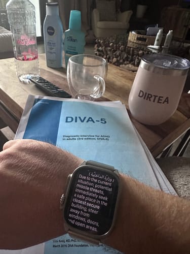 Reviewer's pink DIRTEA tumbler on a table next to an ADHD test and a smartwatch displaying a safety alert.