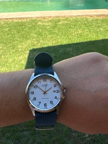Cliente mostrando su reloj Casio analógico en la muñeca, con una correa de tela azul oscuro.