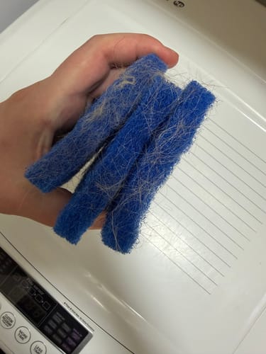 Customer's hand holding several blue Laundry Pet Hair Removal Fish covered in collected pet hair.