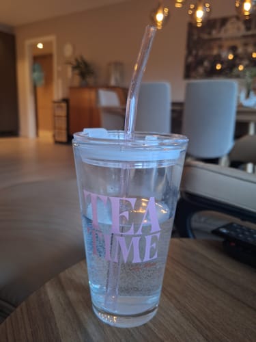 Customer's Tea Time Tumbler Glass with a clear, bubbly drink and glass straw, sitting on a wooden table.