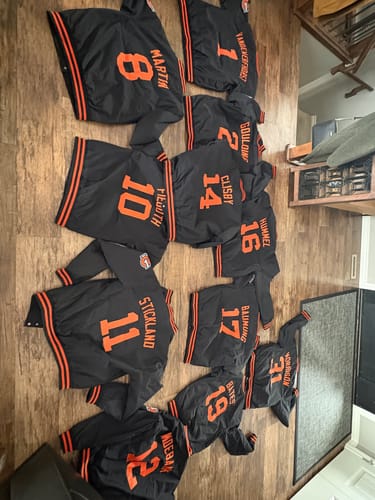 Customer's order of custom black and orange letterman jackets with stitched names and numbers laid out on a wood floor.